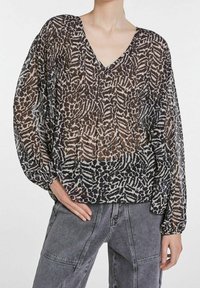 Blusa trasparente con scollatura a V, caratterizzata da un motivo astratto in bianco e nero. Maniche lunghe e morbide con polsini arricciati, texture del tessuto soffice.