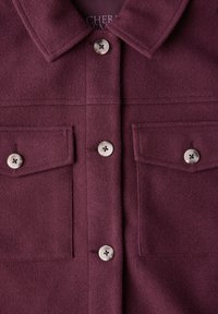 Burgunderfarbener Wollhemdjacke mit spitzem Kragen, zwei vorderen Taschen mit Knopfverschlüssen und strukturiertem Stoff.