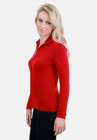 Sweat à zip rouge en tissu doux, avec un col haut et des poches latérales. Conception ajustée avec des manches longues.