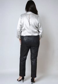 Lichtzijden satijnen blouse met een kraag en een sleutelgatdetail aan de achterkant, gecombineerd met zwarte gestructureerde broeken en zwarte hoge hakken.