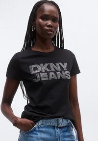 Svart T-skjorte med "DKNY JEANS" i sølv rhinestones over brystet, kombinert med lyseblå denim. Kortermet med rund hals.