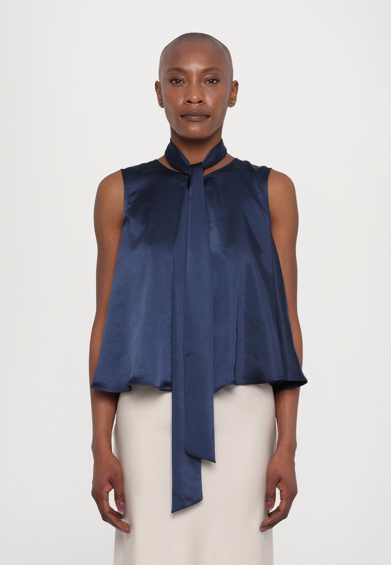 Navy blue satin sleeveless top with a flowing silhouette and a long tie at the neck. Smooth texture with a round neckline and flared hem.