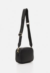 Svart lær crossbody-veske med rektangulær form, teksturert overflate, gullfarget detaljer og justerbar stropp med merkevarenavnet.