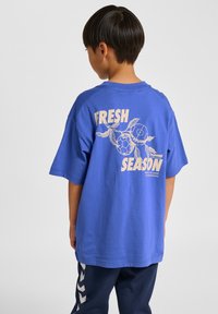 Blå bomulls-T-shirt med avslappnad passform, med en stor krämfärgad grafik på baksidan som inkluderar "FRESH" och ett sköldpaddsmotiv.