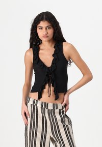 Black sleeveless top with ruffled neckline and drawstring closure, paired with decorative cream and black striped pants.