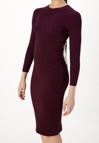 Abito midi in maglia color bordeaux profondo con texture a costine, maniche lunghe e dettagli a linea diagonale che scendono lungo il corpo.