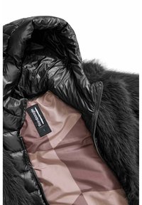 Zwarte pufferjack interior met een glanzende, gladde voering en een zachte, faux fur trim. Etiket zichtbaar aan de binnenkant met maatinformatie.