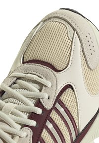 Sneaker mit einem beigen Mesh-Obermaterial, strukturierten Wildlederakzenten, kastanienbraunen Kunststoffstreifen und hellen Schnürsenkeln. Verfügt über eine gepolsterte Sohle für Komfort.