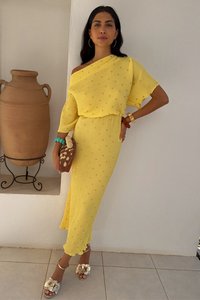 Geel geribbelde jurk met gouden accenten, off-shoulder ontwerp, tot op de knie, gecombineerd met versierde sandalen en een geweven handtas.