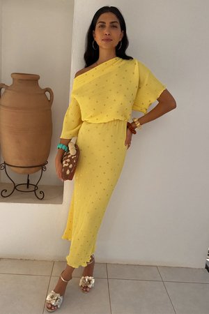 Yellow ribbed dress with gold accents, off-shoulder design, knee-length, paired with embellished sandals and a woven handbag.