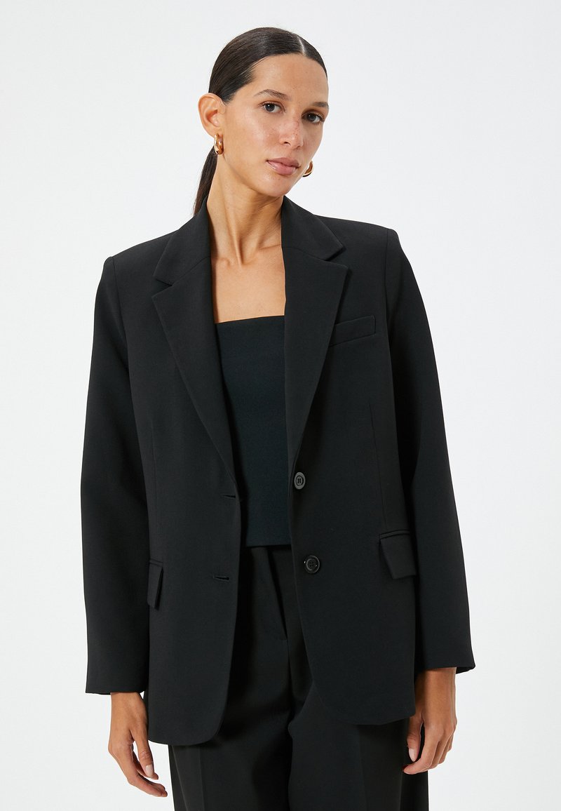 Blazer nero realizzato in tessuto liscio, con chiusura a due bottoni e un solo petto, revers a punta e una tasca frontale; vestibilità rilassata.
