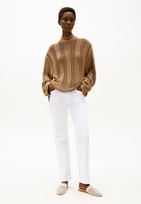 Suéter de punto grueso en color beige con rayas verticales, de cuello alto; combinado con pantalones blancos ajustados y zapatos de piel texturizados de color marrón claro.
