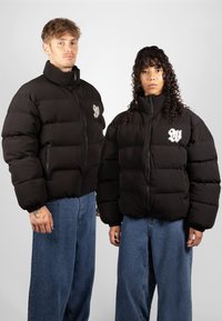 Black puffer jackets with a high collar and zip front, featuring horizontal quilted sections and white embroidered logo accents.