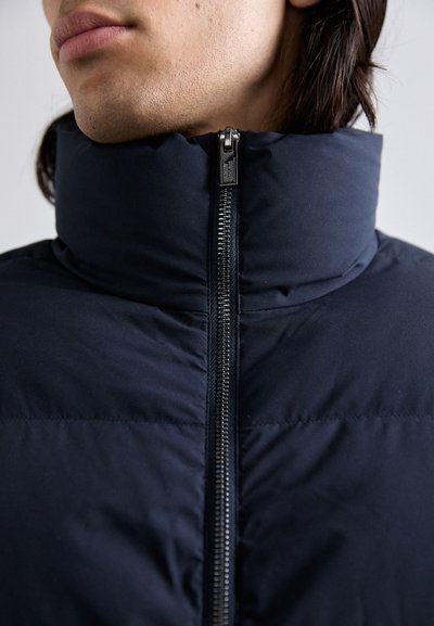 Mørkeblå dunjakke med høj krave, fuldlængde lynlås og quiltet struktur. Glat stof med mat finish, minimale hardware detaljer.