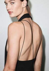 Vista trasera de un vestido negro sin mangas con tirantes finos, que revela un diseño de espalda descubierta y una textura suave sobre un fondo neutro.