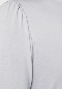 Haut court à manches courtes gris clair avec des épaules froncées, fabriqué en tissu doux et extensible. Texture lisse avec des coutures minimales et sans motifs visibles.