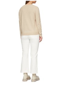 Pull beige avec un col rond, une texture douce et des manches longues, assorti à un pantalon blanc évasé et des bottines beige à semelle épaisse.