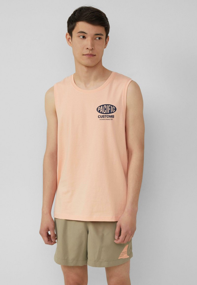 Lichtroze mouwloos topje met het "PACIFIC CUSTOMS" logo in marineblauw, gecombineerd met licht kaki shorts met een klein logo patch.