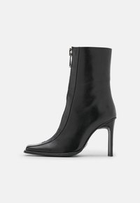 Bottine en cuir noir avec bout pointu, fermeture éclair latérale et talon haut fin, présentée de profil sur un fond uni.