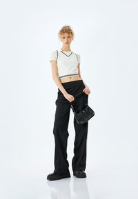Wit cropped top met zwarte randen, losse zwarte broek en een kleine zwarte tas. De outfit heeft een sportief ontwerp en textuurmaterialen.