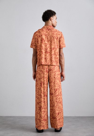 Short-sleeved, collared shirt and wide-leg trousers in orange and terracotta with a leafy pattern; lightweight fabric and relaxed fit.