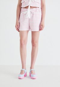 Tweedshorts i rosa og hvitt med rutemønster, med elastisk midje og to frontlommer, kombinert med pastellfargede platåsko.