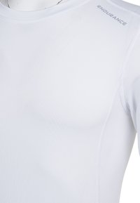 T-shirt de sport blanc en tissu lisse et respirant. Présente des coutures plates et le mot "ENDURANCE" en argent sur l'épaule.
