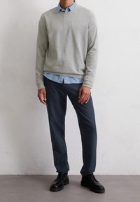 Sudadera gris combinada con una camisa de cuello azul claro, acompañada de pantalones oscuros y zapatos negros con cordones. Texturas suaves y tonos neutros.