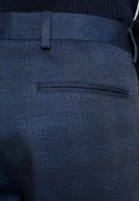 Navy blue tailored trousers with a subtle geometric pattern, featuring a back pocket and a smooth texture. Adjustable waistband detail.