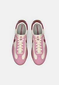 Pink and cream sneakers with a suede and synthetic upper, featuring flat laces, a rubber sole, and "CONVERSE" branding in red.