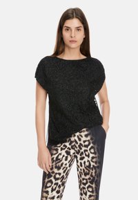Schwarzes Oberteil mit floralem Perlen-Detail, kurzen Ärmeln und lockerem Schnitt, kombiniert mit gemusterten Leopardenprint-Hosen. Glatte Textur über das gesamte Kleidungsstück.