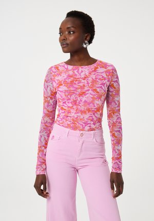 Langarm T-shirt van doorschijnende roze stof met een bloempatroon in roze en oranje tinten, gecombineerd met lichtroze hoge taille jeans.