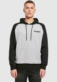 Grauer und schwarzer Hoodie mit einer Kängurutasche auf der Vorderseite, Kordeln und dem Schriftzug "Compton" auf der oberen linken Brust in Schwarz. Weicher Stoff.