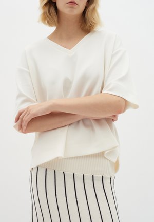 White V-neck oversized top, soft fabric, short sleeves, layered design, paired with a cream and black striped knit skirt.