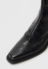 Schwarze Leder-Ankle-Boots mit Krokodilstruktur, spitzem Zeh, dezenten Nähten und einer flachen Gummisohle. Reißverschlussdetails an der Seite.