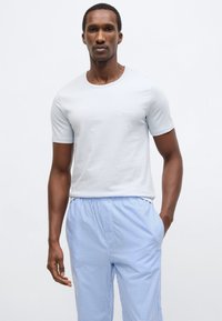 Vaaleansininen lyhythihainen t-paita pyöreällä kaula-aukolla ja hillityllä "BOSS"-logolla, yhdistettynä vaaleansinisiin ruudullisiin olohousuihin.