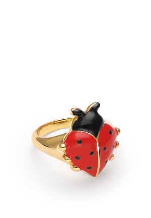 Anillo de oro con un diseño de mariquita roja y negra con manchas negras y detalles dorados sobre un fondo blanco.