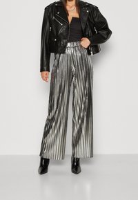 černá kožená zkrácená bunda s širokými kalhotami z metalického stříbra s plisováním. Kalhoty mají svislé pruhy a vysoký pas. Černé špičaté boty.