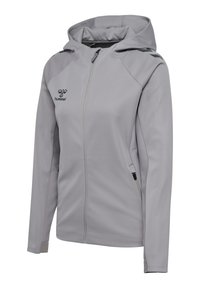 Giacca grigia chiara con zip e cappuccio, caratterizzata da una texture liscia, logo nero e dettagli sulle spalle, due tasche laterali e polsini aderenti.