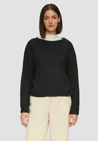 Zwarte sweatshirt met lange mouwen, een ronde hals en een relaxte pasvorm, gemaakt van zacht materiaal, gecombineerd met lichtbeige broek.