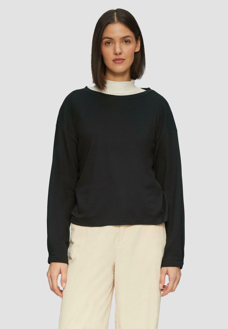 Zwarte sweatshirt met lange mouwen, een ronde hals en een relaxte pasvorm, gemaakt van zacht materiaal, gecombineerd met lichtbeige broek.