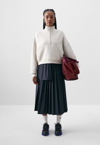 Bela blagovna majica s četrtinskim zadrgo, mornarsko modra plisirana krila, črne superge s vijoličnimi poudarki in bordo torba z stranskimi žepi.