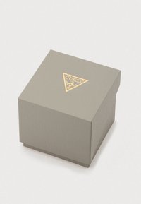 Grå gaveæske med ribbet tekstur og et gyldent trekantet logo på toppen. Firkantet form med låg, der passer tæt.