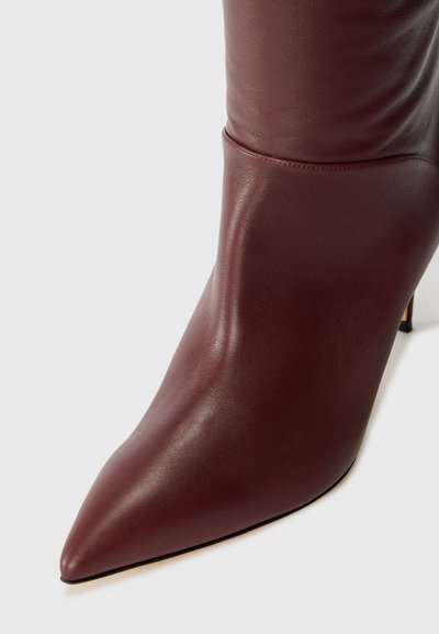 Bottine en cuir bordeaux avec un bout pointu et une silhouette épurée. Présente une texture lisse et un talon aiguille, mettant en valeur un design moderne.