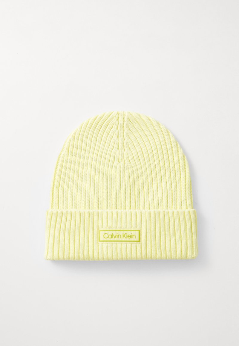 Yellow ribbed knit beanie with a folded cuff and a rectangular Calvin Klein logo tag in a contrasting shade. Soft, textured fabric.