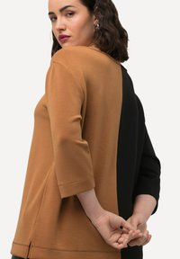 Dvoudílný top s hnědo-černým designem. Vyroben z jemné látky, s volným střihem a tříčtvrtečními rukávy. Jednoduché švy.