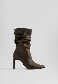 Brun læder ankelstøvle med et slouchy design, spids tå og en stiletto hæl. Glat tekstur med subtile folder.