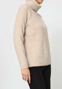 Pull à col roulé côtelé beige en tissu doux, doté de manches longues, d'une coupe ajustée et d'une silhouette décontractée.