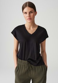 Schwarzes, kurzärmeliges V-Ausschnitt-T-Shirt aus glattem Stoff, kombiniert mit olivgrünen, locker sitzenden Hosen mit Gummizug.