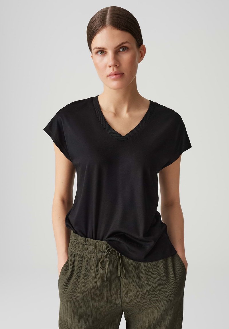 Schwarzes, kurzärmeliges V-Ausschnitt-T-Shirt aus glattem Stoff, kombiniert mit olivgrünen, locker sitzenden Hosen mit Gummizug.